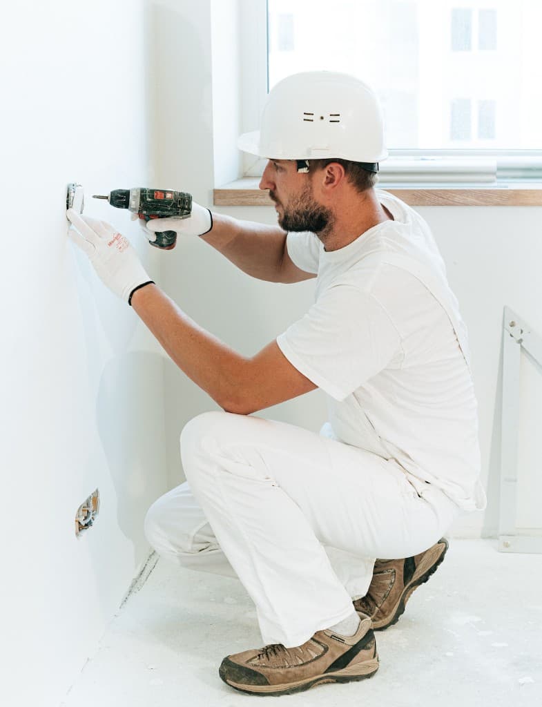 Electrician installing a residential wall outlet with a power drill
