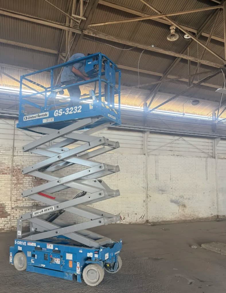 Electrician installing high-bay lighting from a scissor lift in a commercial building