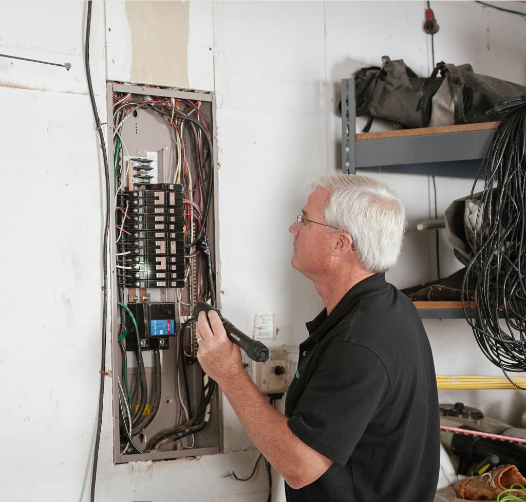 Electrician inspecting a residential electrical panel with a flashlight