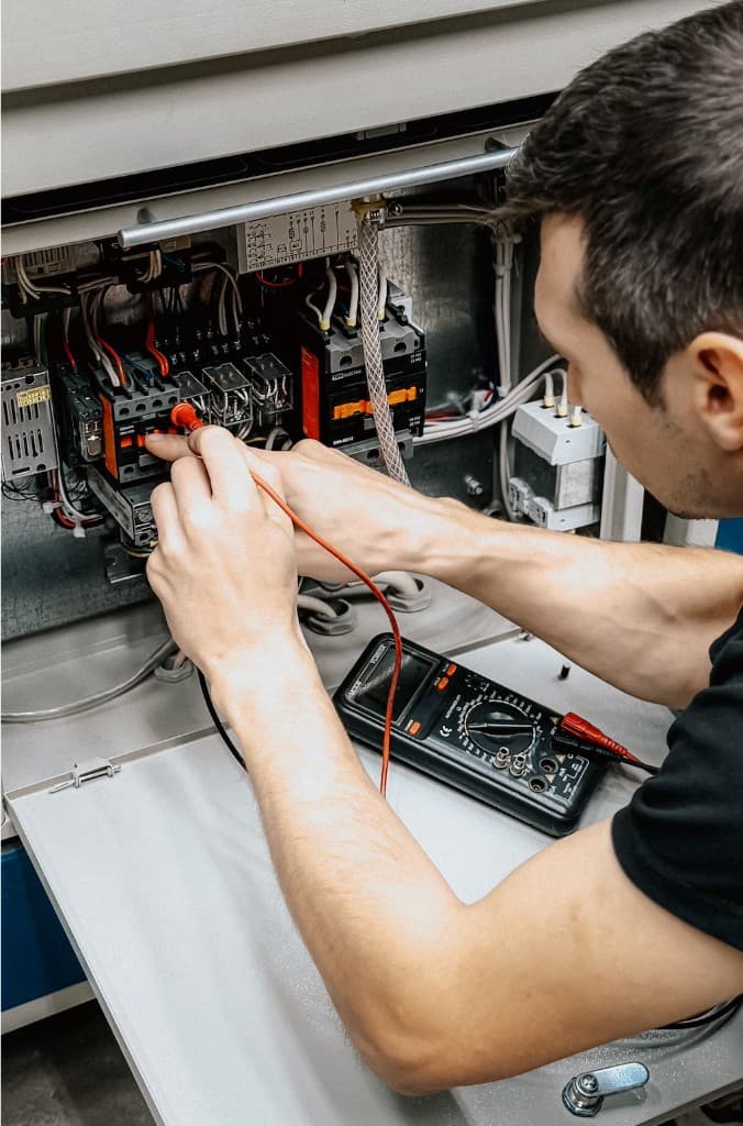 Electrician troubleshooting a control panel with a digital multimeter